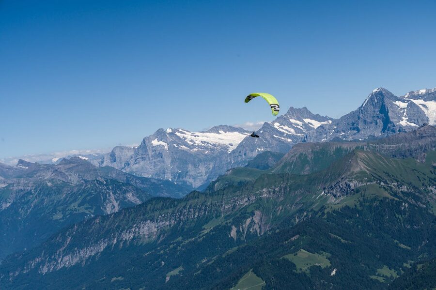 Paraglider flying over green Swiss Alps on a clear summer day