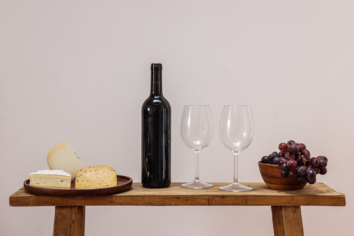 Wine bottles and glasses on a wooden table with cheese and grapes