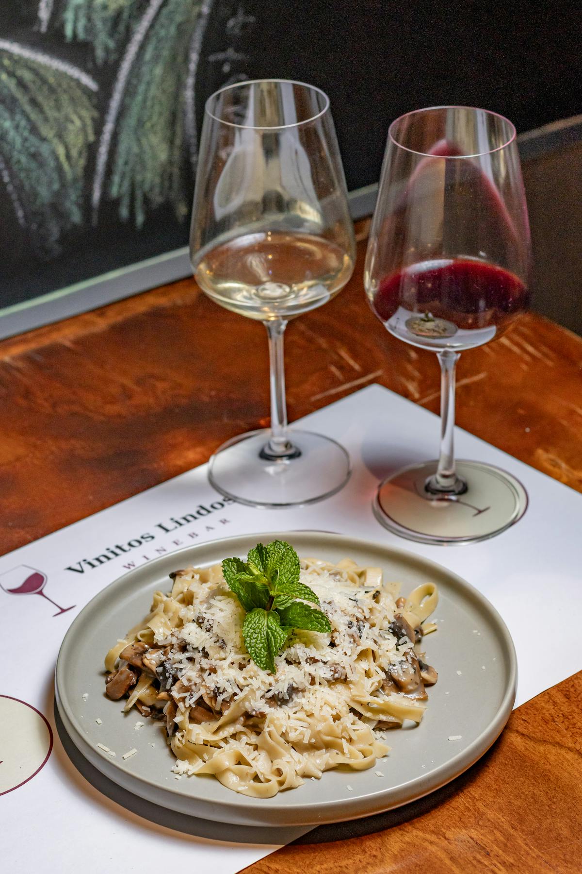 Plate of creamy pasta garnished with mint next to glasses of wine on a dinner table