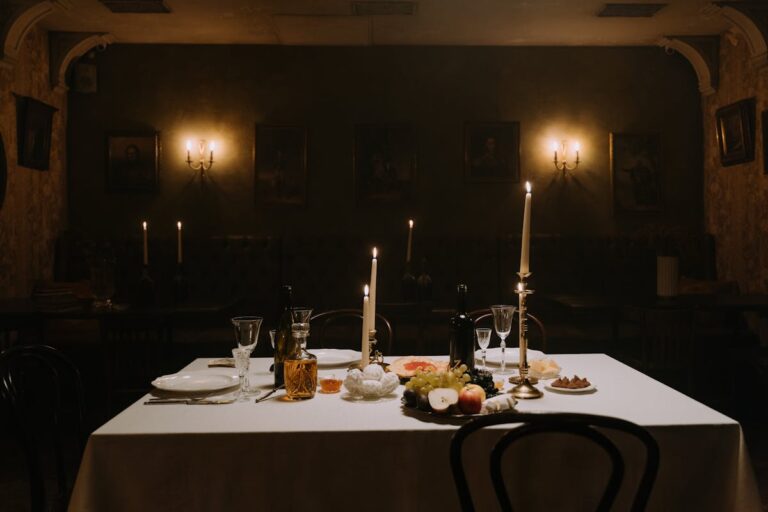 Long wooden table with candles, wine goblets, and fruit in a dimly lit medieval dining room