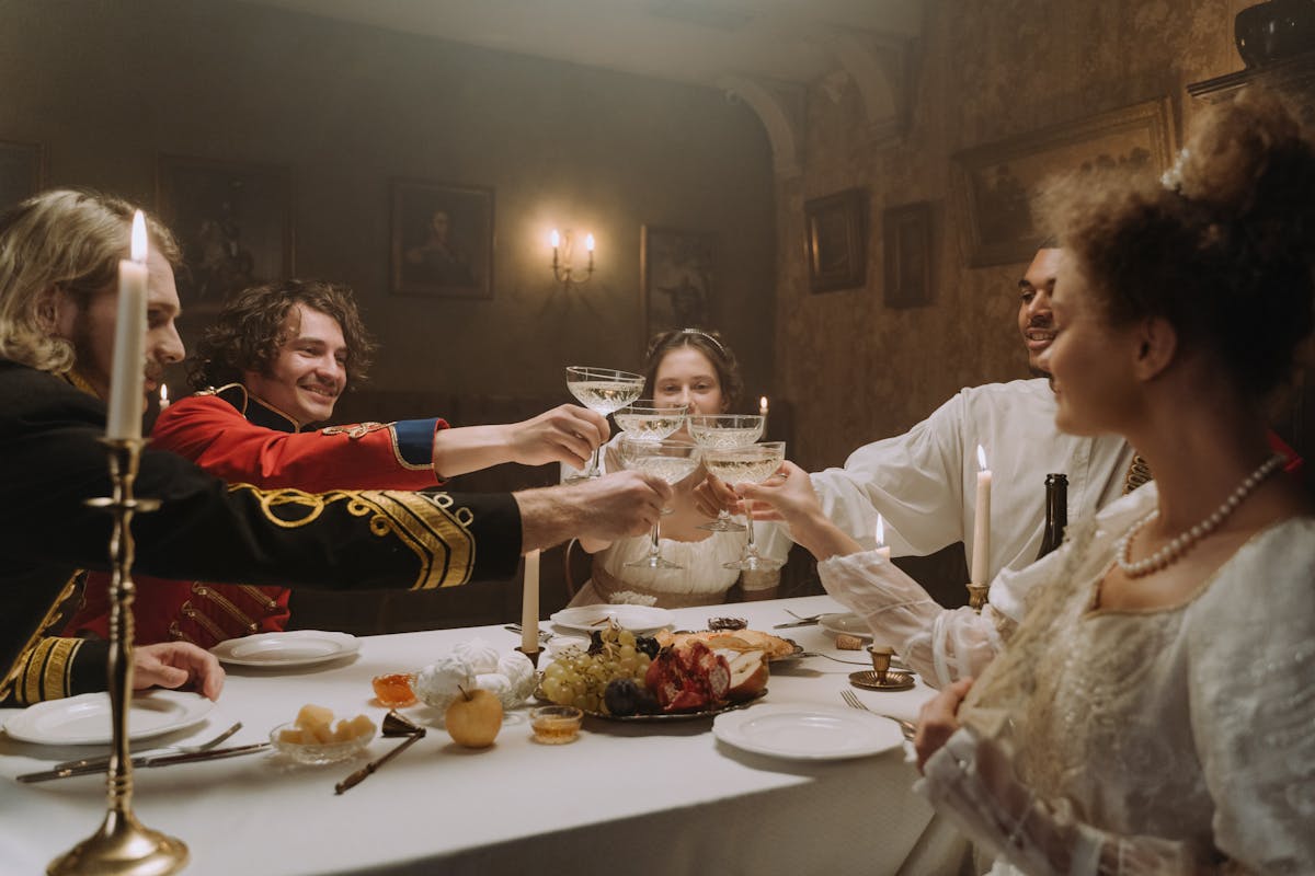 People in period costumes toasting wine glasses at a festive candlelit dinner