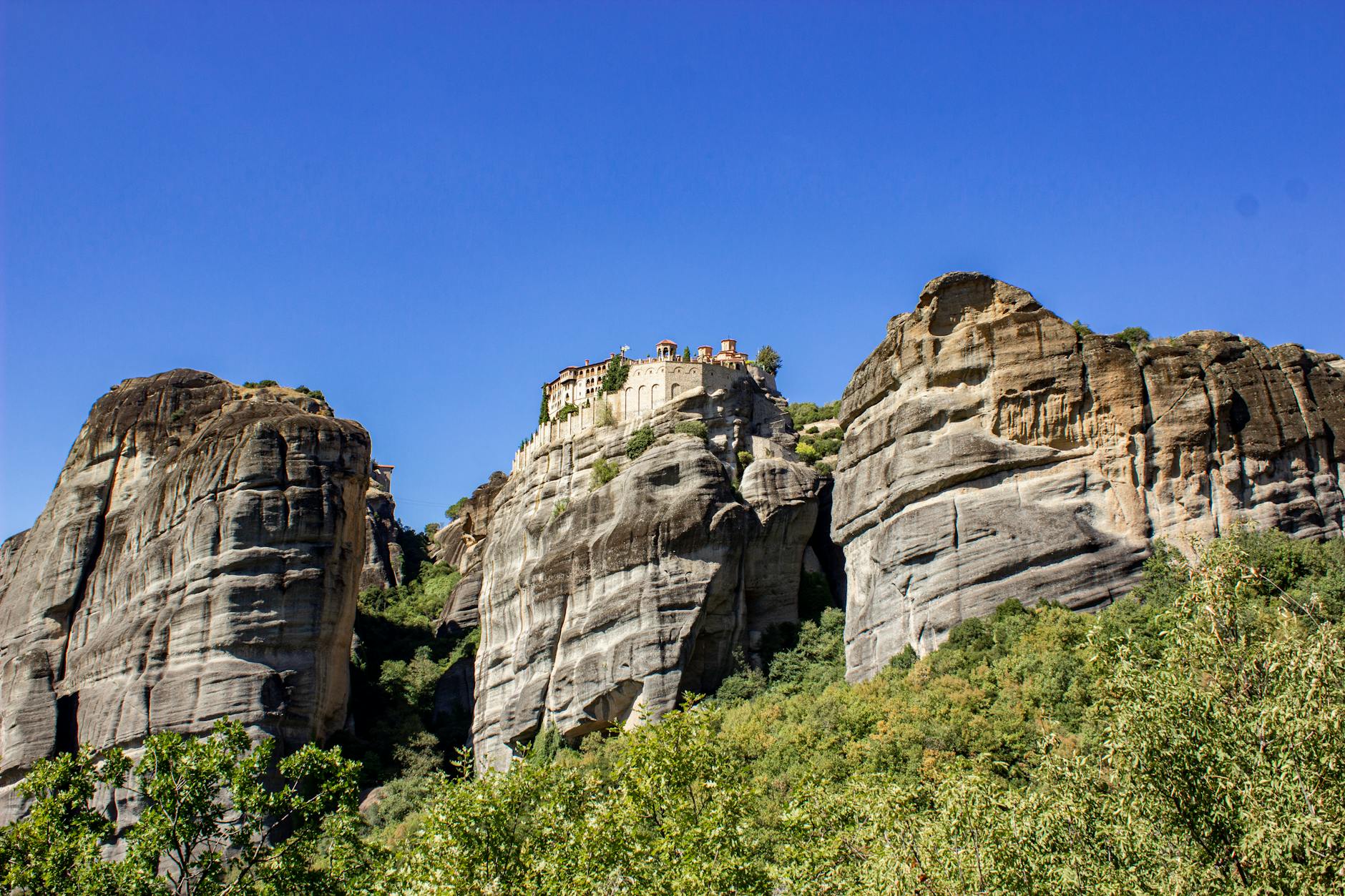 Majestic view of a Meteora monastery perched on massive rock formation under blue sky in Greece