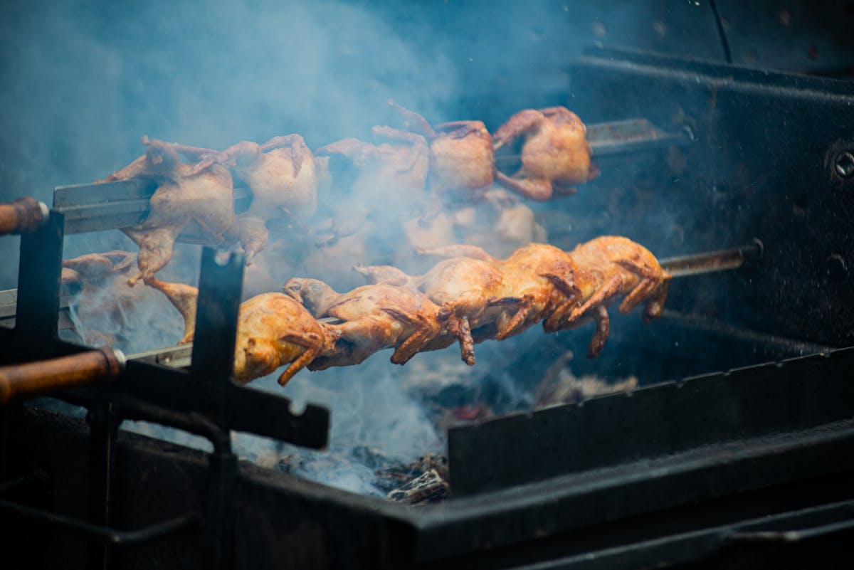Whole chickens rotating on a spit roast over open flames outdoors