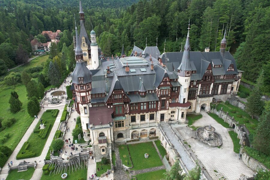 Aerial view of Peles Castle surrounded by green forests in Romania