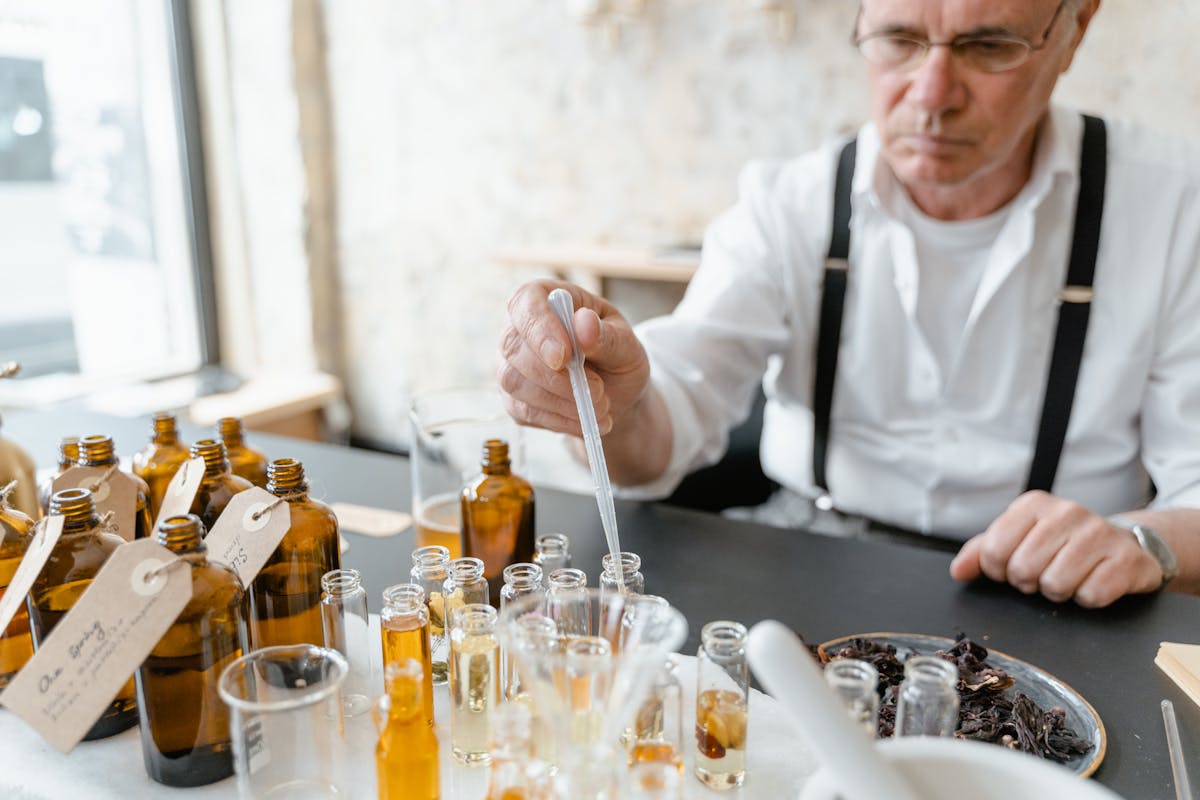 Senior male perfumer preparing natural fragrance mixtures at workbench with lab tools