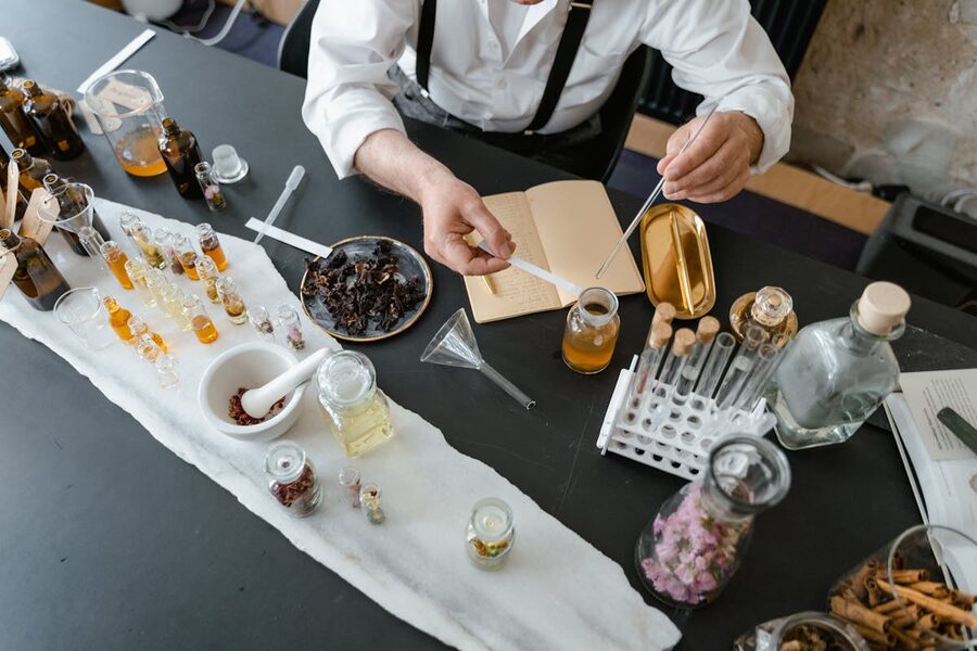 Artisanal perfume-making setup with notebook, flowers, and glass bottles on workbench