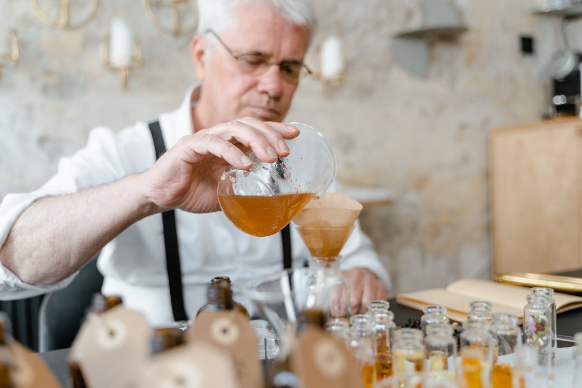 Person pouring brown liquid into a glass bottle during a perfume creation workshop