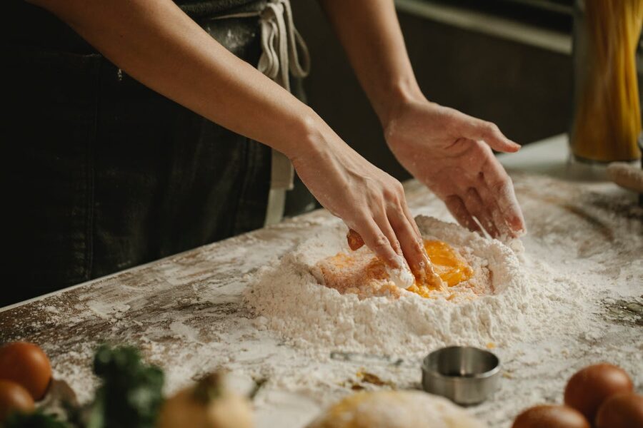 Hands shaping fresh pasta dough on a floured wooden surface