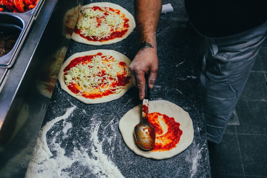 Chef spreading tomato sauce on pizza dough in kitchen