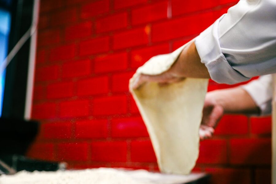 Chef skillfully stretching pizza dough in a red brick kitchen
