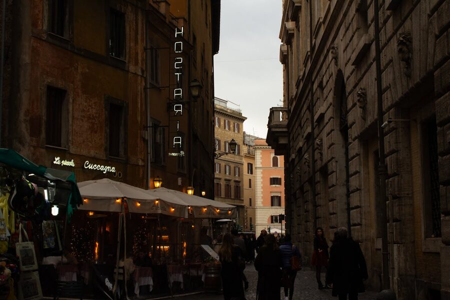 Narrow street in Rome lined with restaurants and warm evening lighting