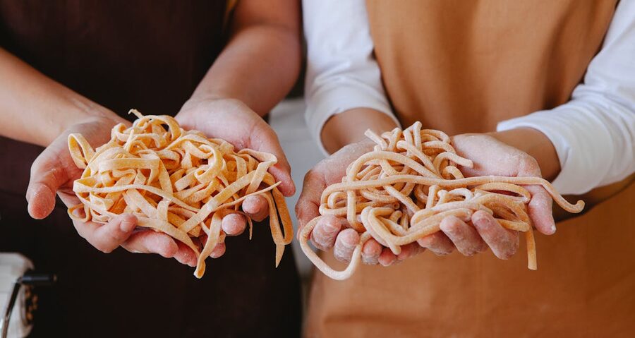 Two people displaying freshly made pasta strands