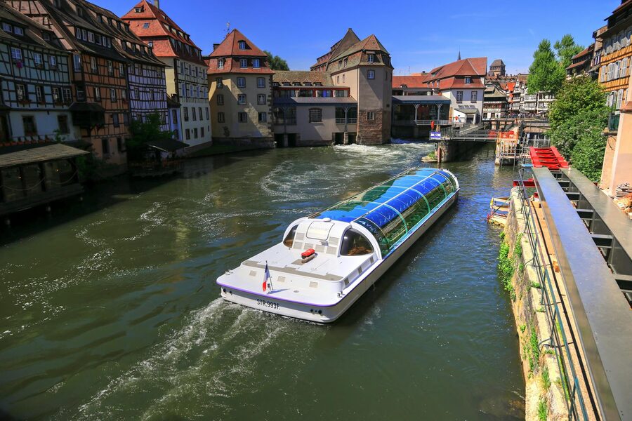 A modern boat sailing through the canals of Strasbourg with traditional half-timbered buildings on both sides