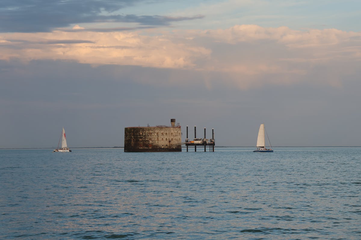 Sailboats passing by a stone fortification on the Charente-Maritime coast