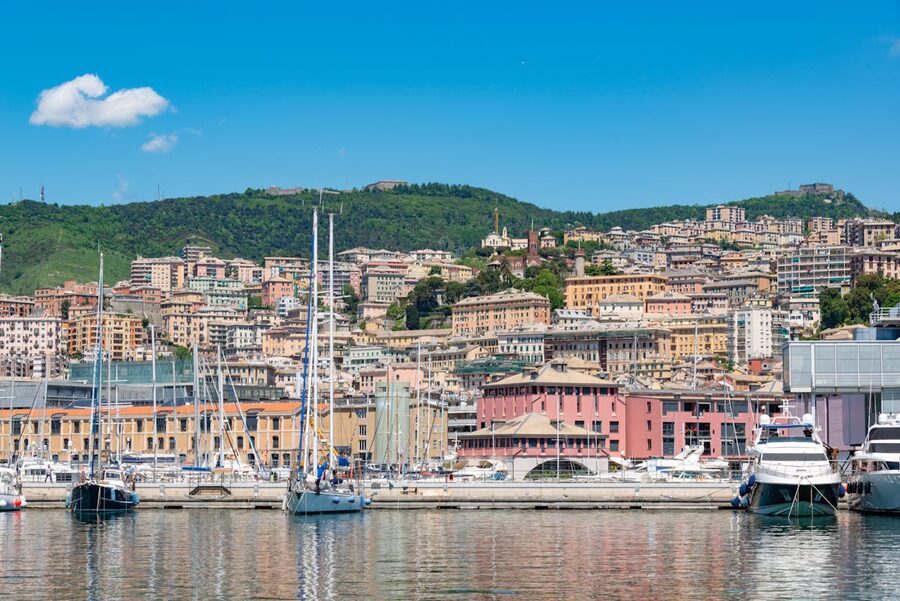 Sailboats moored in Genoa marina with the colourful hillside townscape in the background