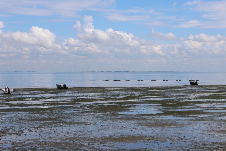 Peaceful seascape with boats on calm water and clouds reflecting on the sea