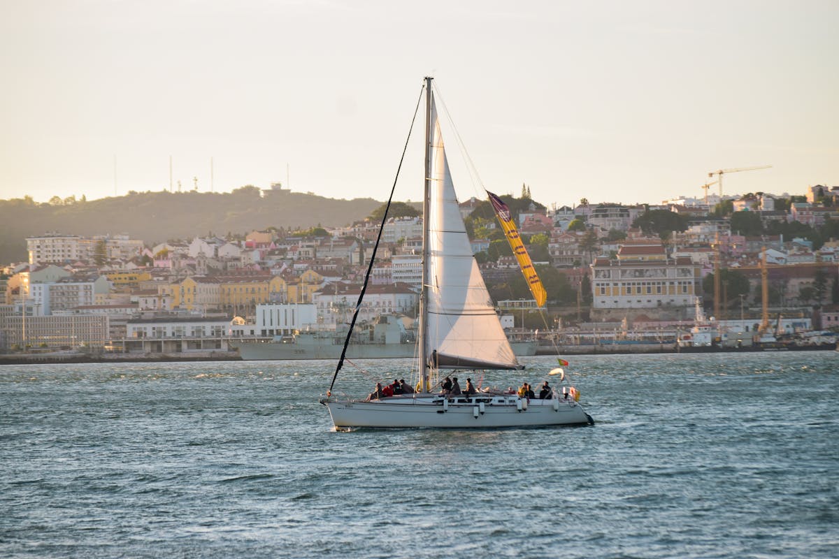 A sailboat cruises along the Lisbon waterfront with the city in the background