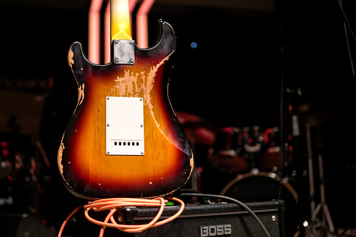 A worn electric guitar resting on an amplifier on a dimly lit stage