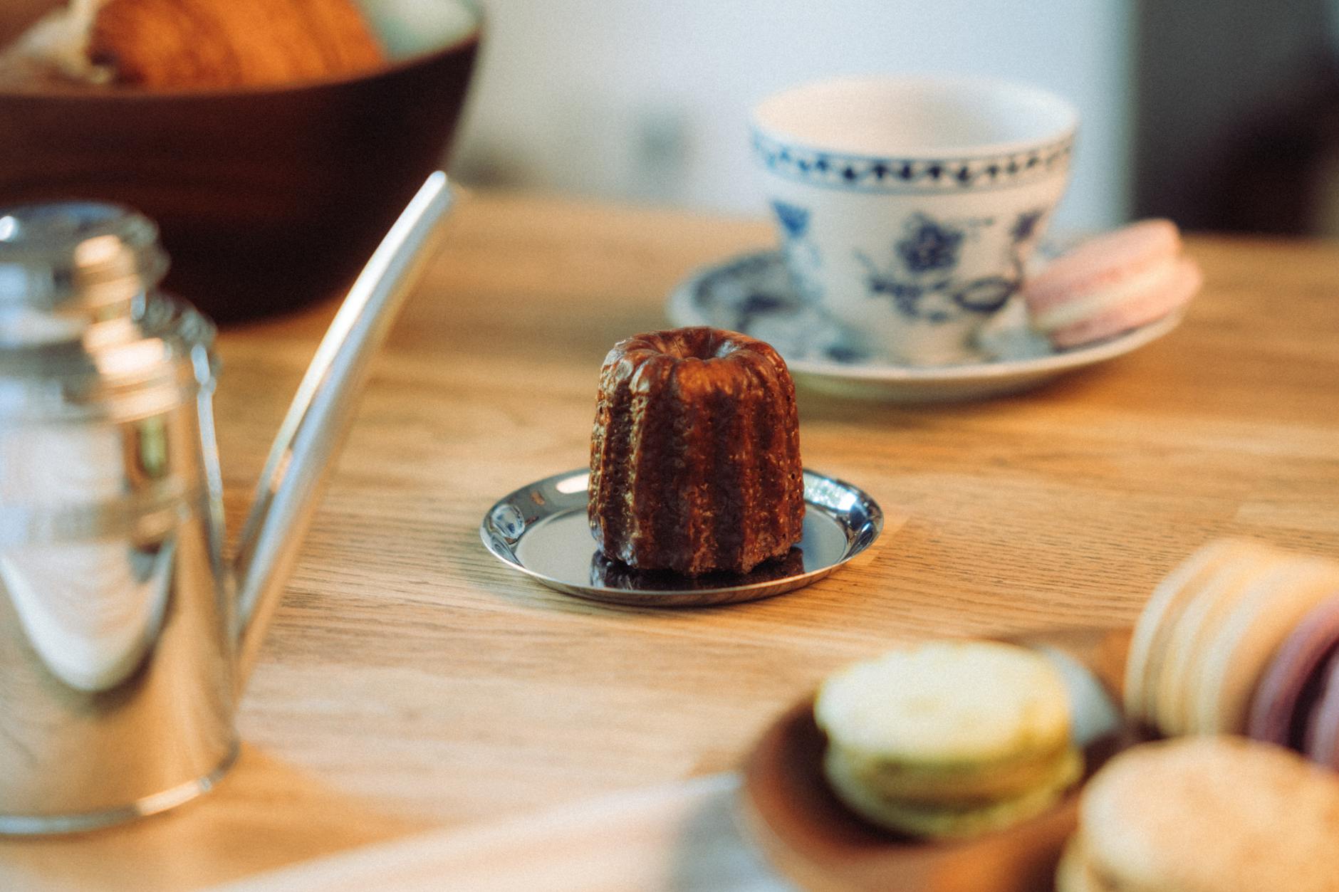 A cozy French patisserie setup featuring a canele macarons and a tea set on a wooden table