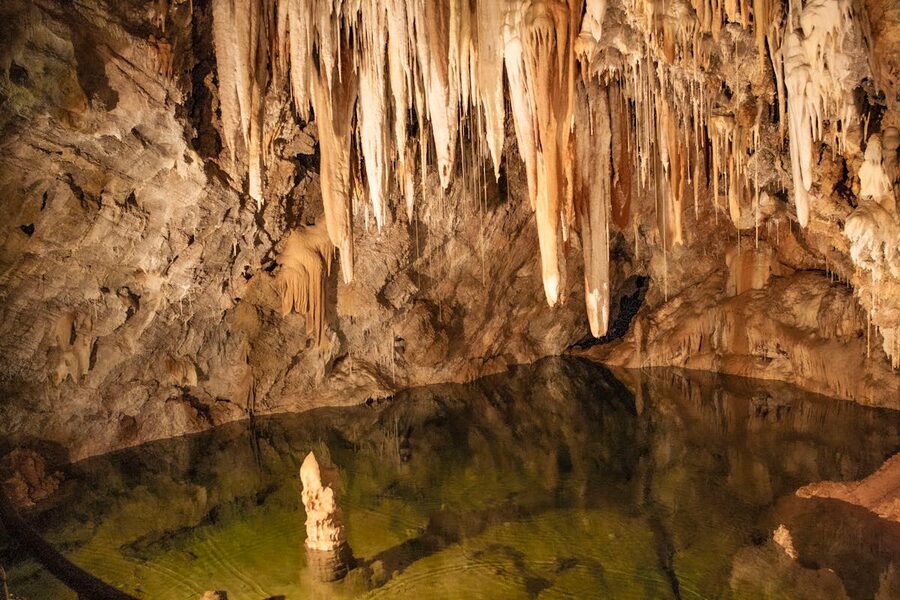 A vast underground cave with stalactites reflected in a still pool of water