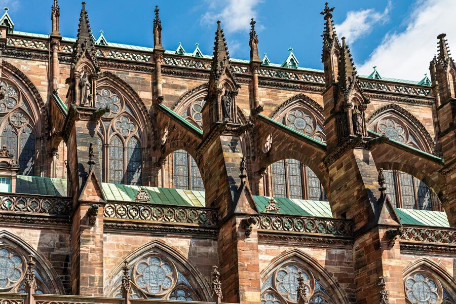 The ornate Gothic facade of Strasbourg Cathedral with its single spire against a clear blue sky