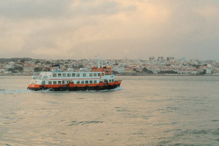 A ferry crosses the Tagus River with the Lisbon skyline glowing at dusk