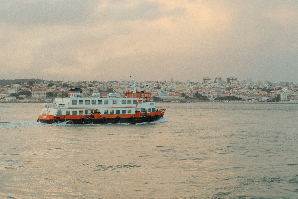 A ferry crosses the Tagus River with the Lisbon skyline glowing at dusk