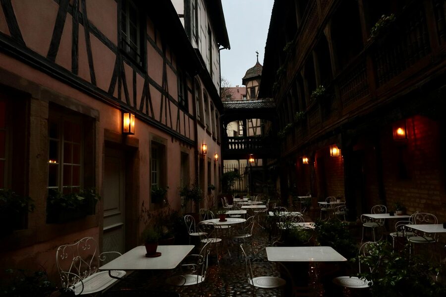 A dimly lit courtyard with tables and chairs beneath lanterns in historic Strasbourg