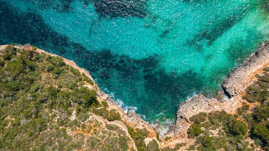 Drone shot of rocky cliffs meeting clear turquoise sea waters in Mallorca
