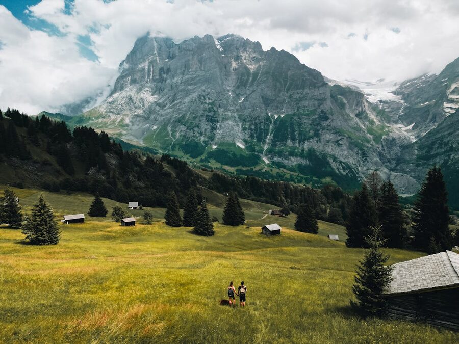 Two hikers walking along a mountain trail with panoramic Swiss Alps views