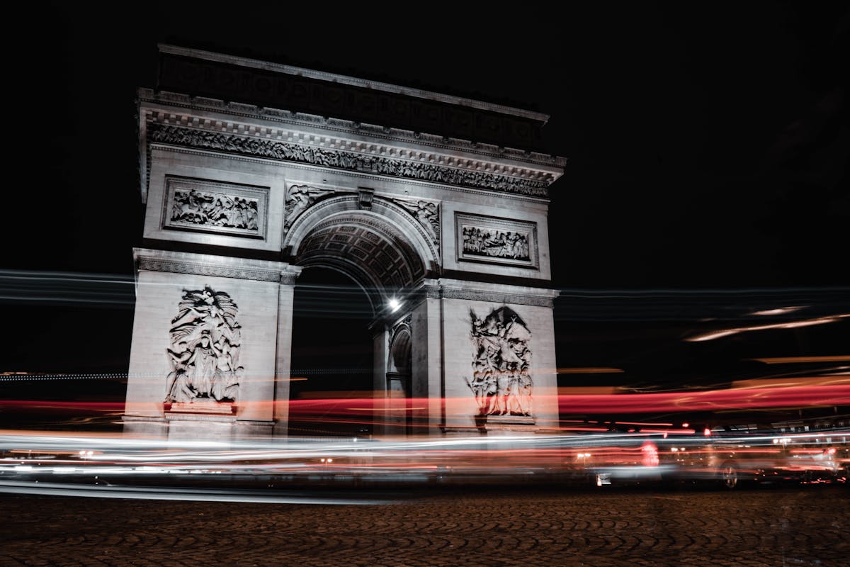 Dramatic night shot of the Arc de Triomphe with car light trails streaming around the roundabout