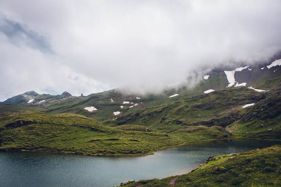 Alpine lake Bachalpsee with green meadows and mountains under overcast skies