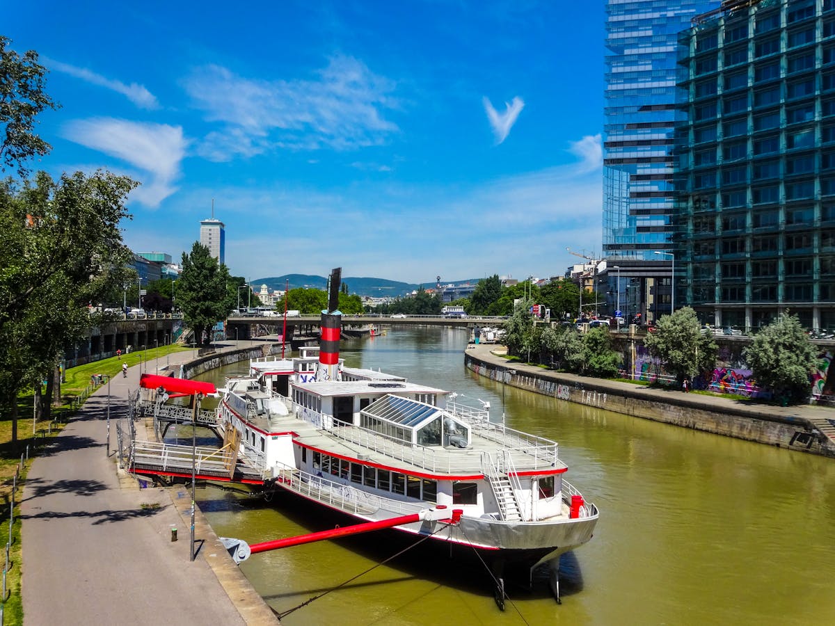 A modern boat docked on the Danube Canal in Vienna with the urban cityscape behind