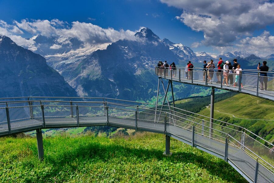 Tourists standing on a panoramic bridge with mountain views at First above Grindelwald
