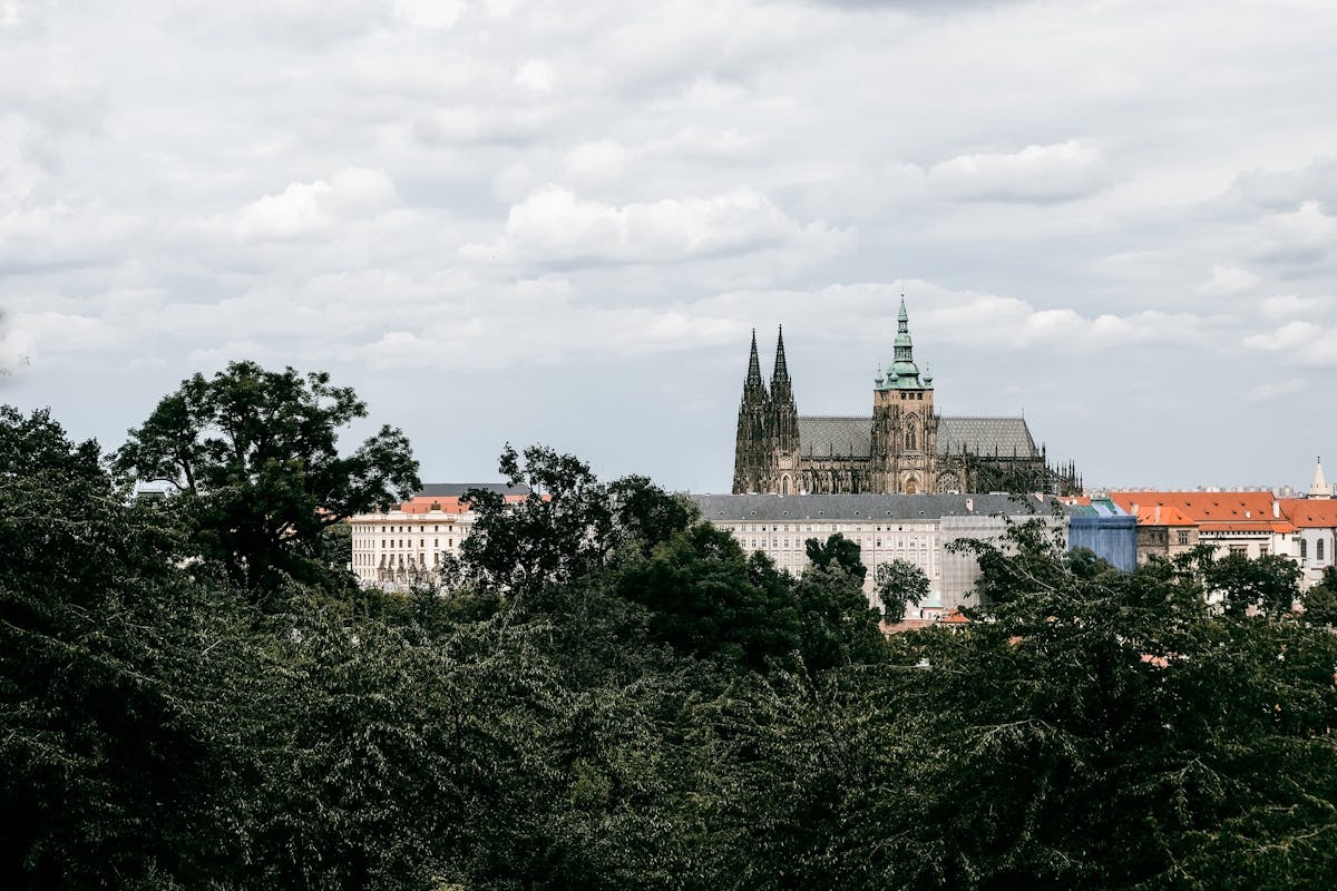Prague Castle with lush green gardens and trees under a cloudy sky