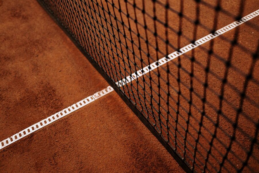 Close up of tennis net with chain link on a clay court surface
