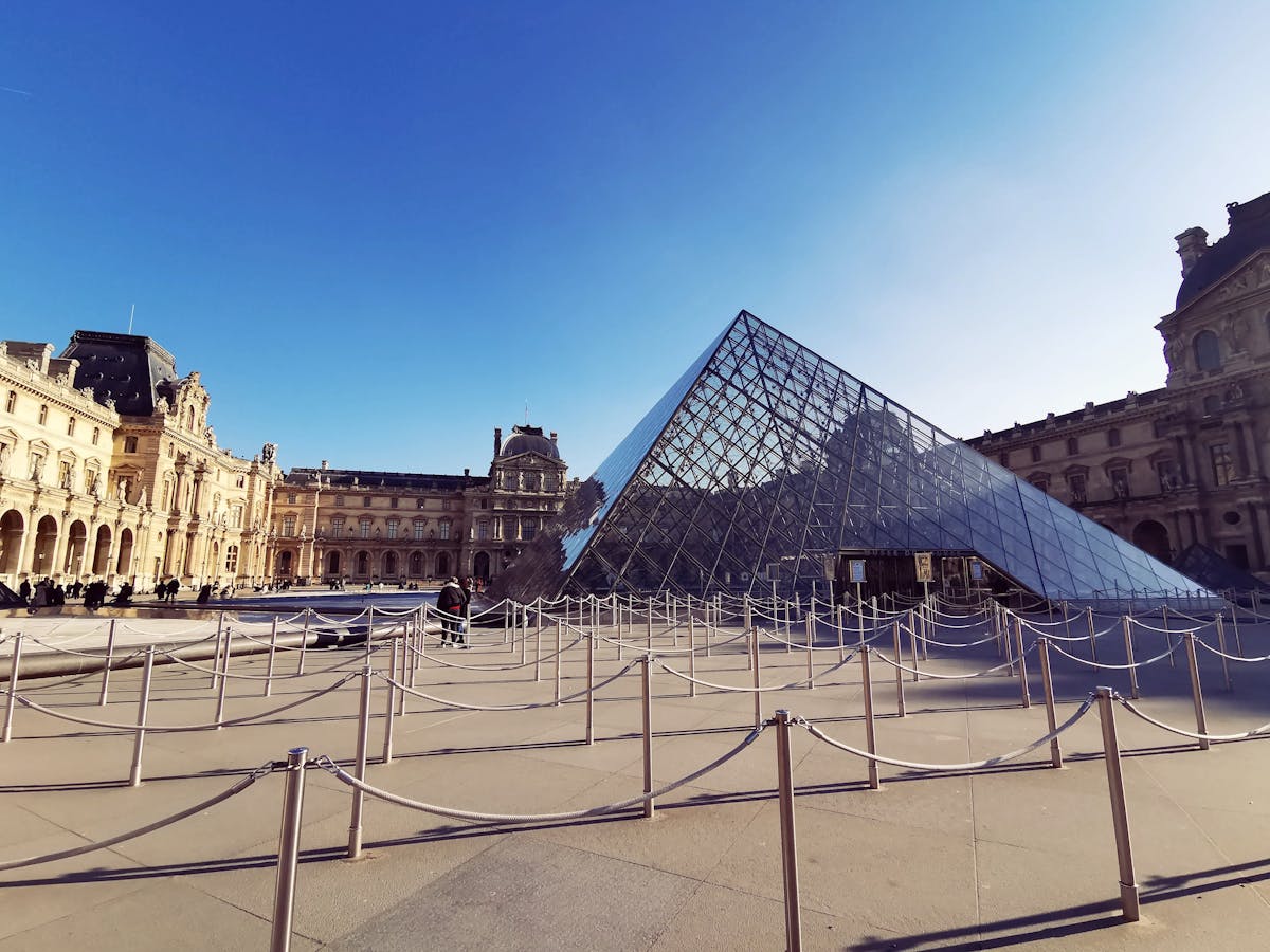 The glass Louvre Pyramid under a bright blue sky with the palace wings framing it