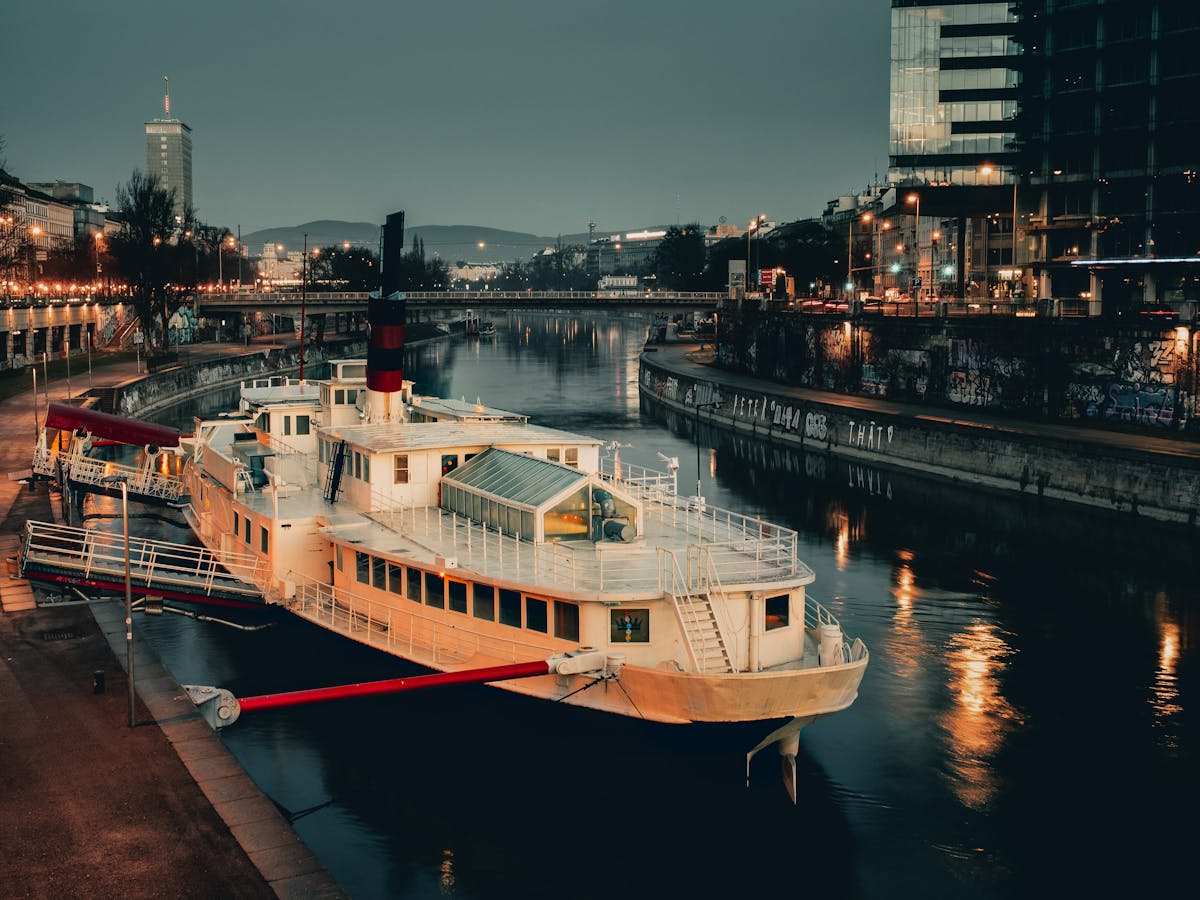 A serene night scene of a docked boat on the Donaukanal in Vienna with urban reflections