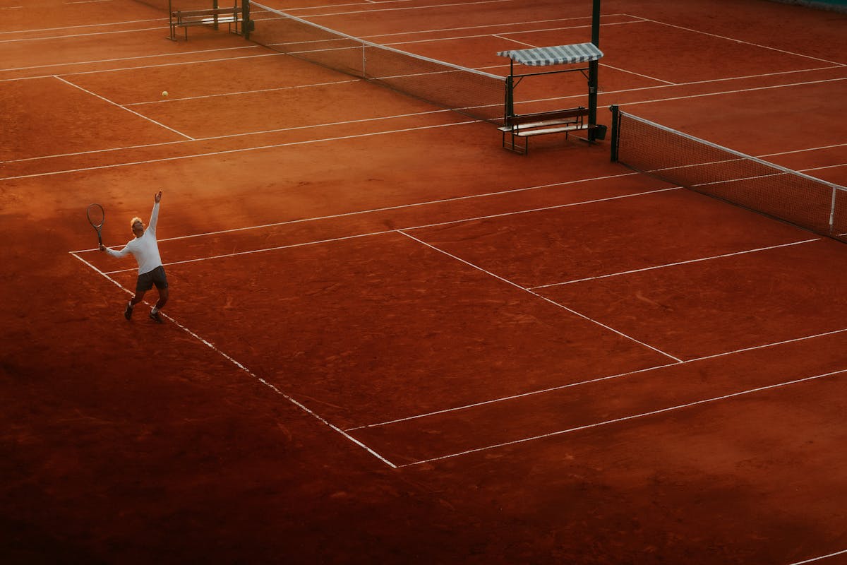 Silhouette of tennis player serving on clay court in fading light