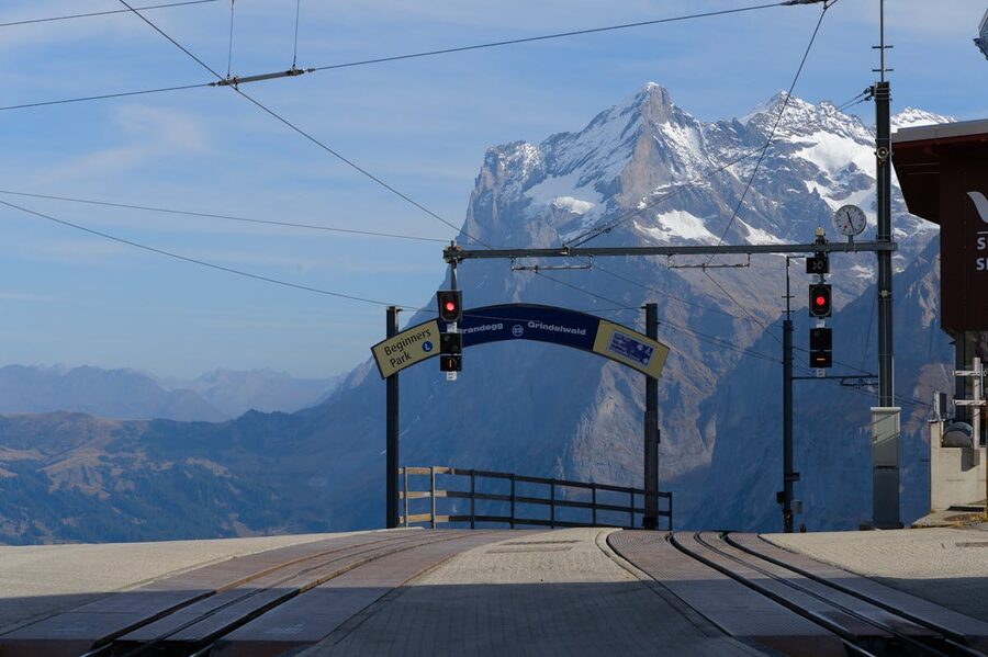 Train station platform with red Swiss train and dramatic Alpine mountains in the background
