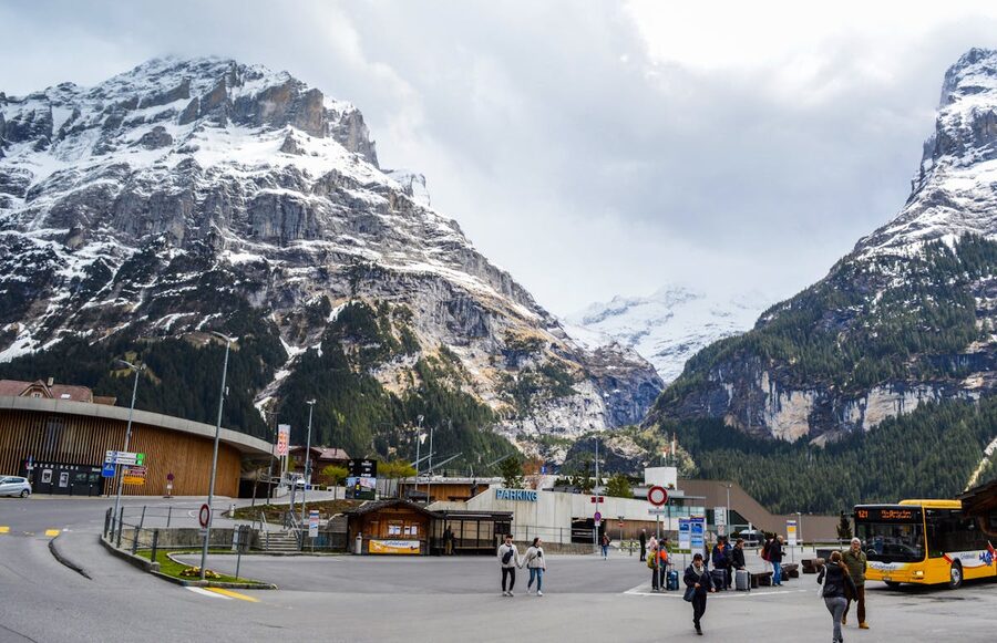 People walking on a village road with snow-covered mountains in the background