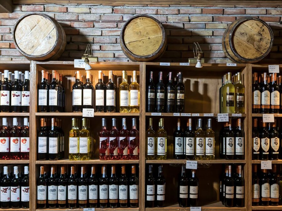 Rustic wine cellar with rows of wine bottles and wooden barrels against brick walls