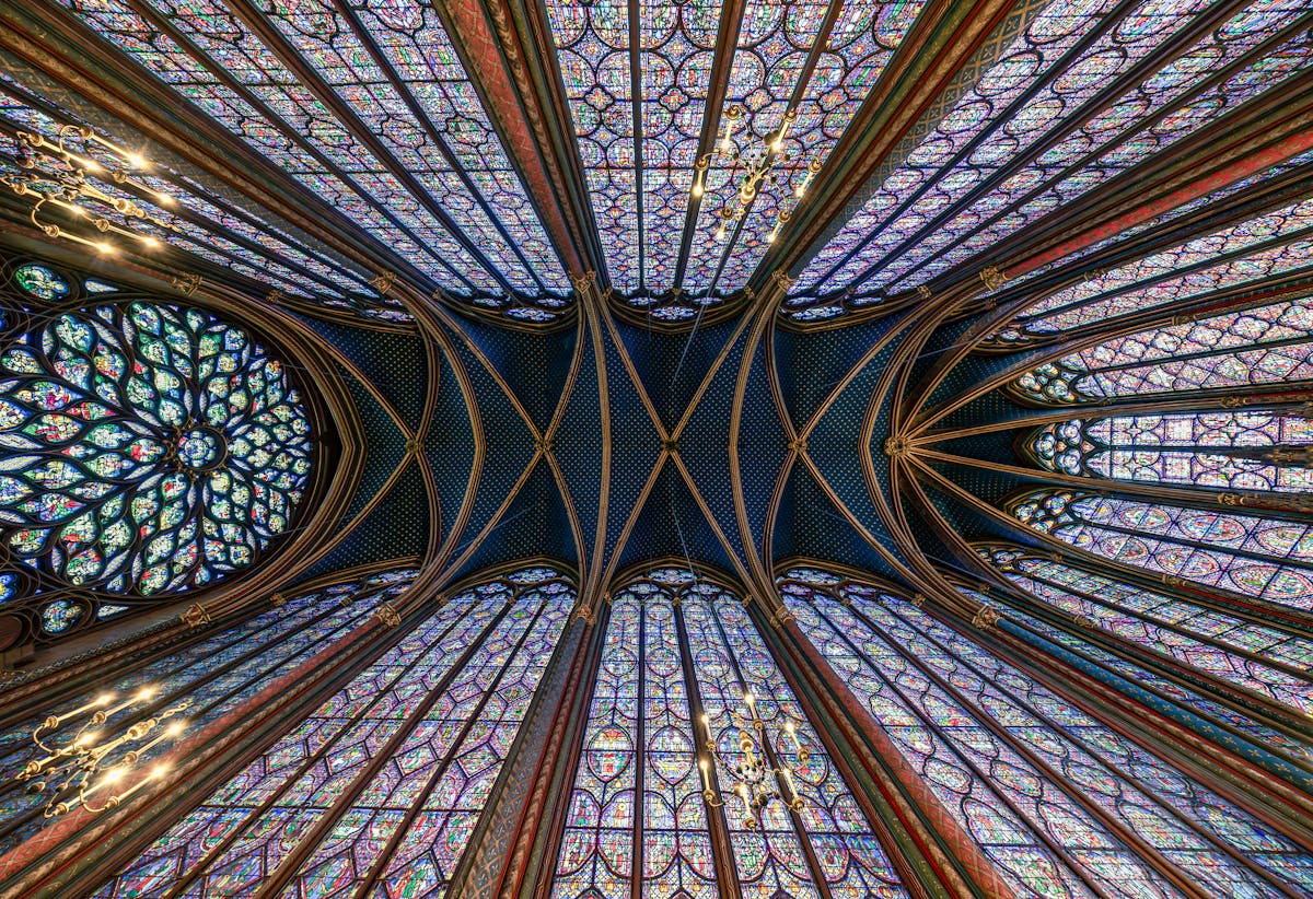 Looking up at the Gothic ribbed ceiling of Sainte-Chapelle with stained glass on all sides