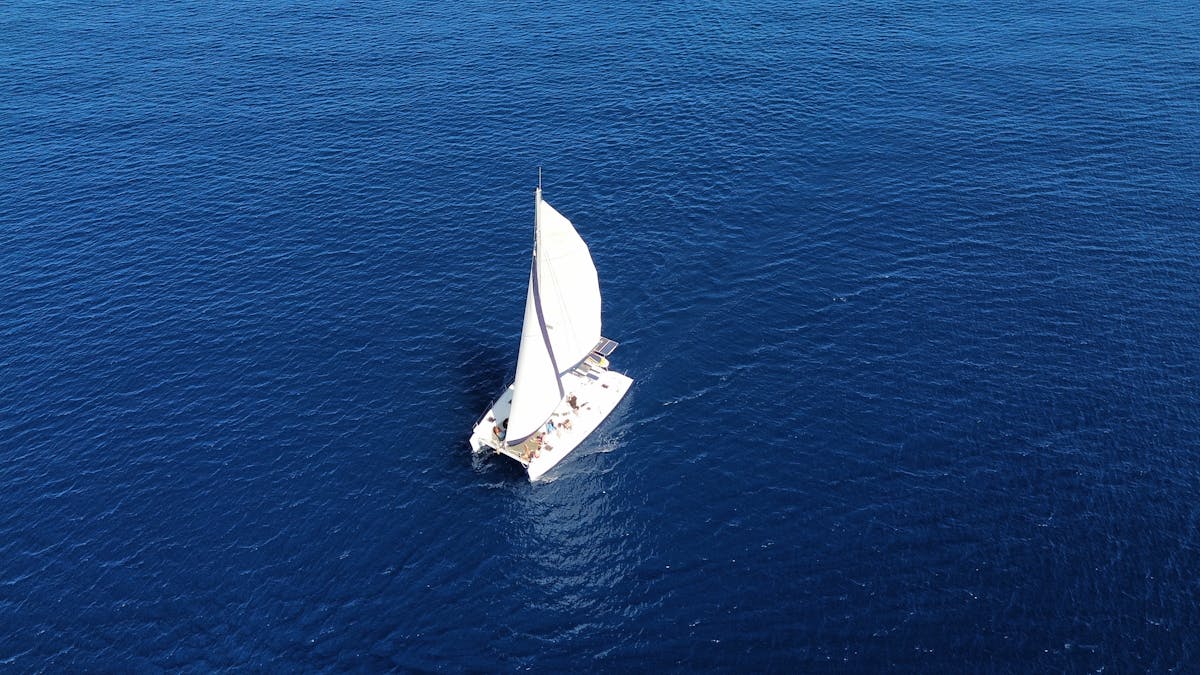 Aerial shot of a sailboat navigating through the deep blue sea