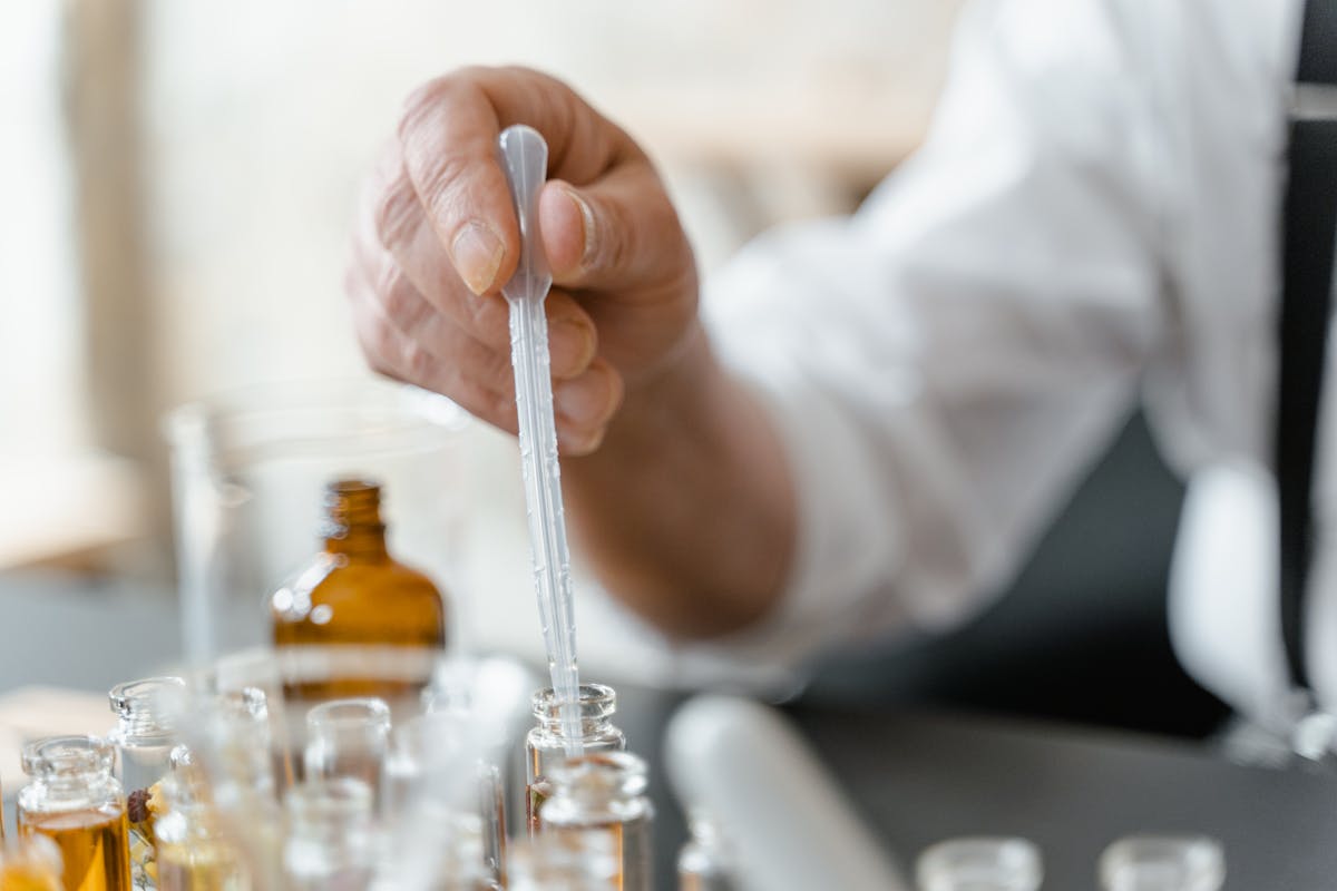 Detailed image of person mixing essential oils in glass tubes in laboratory setting