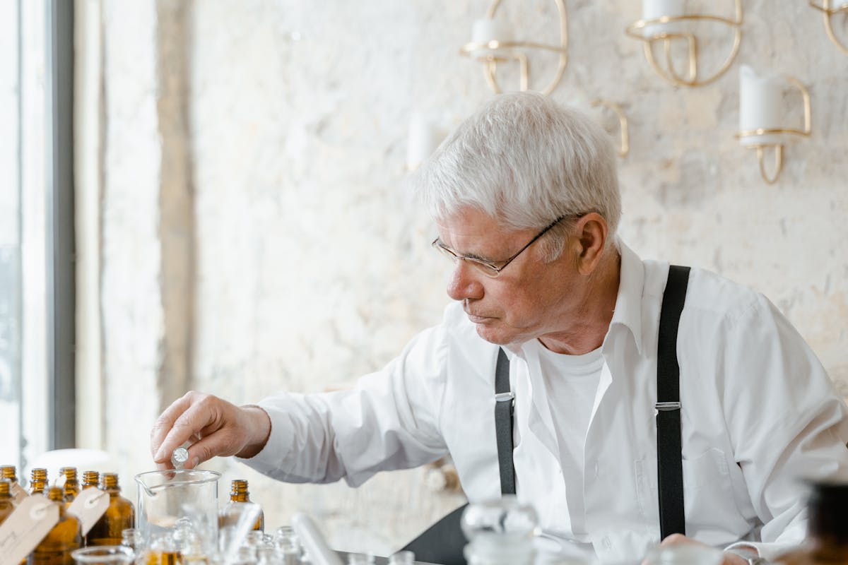 Senior perfumer with glasses working with perfume bottles at his workstation
