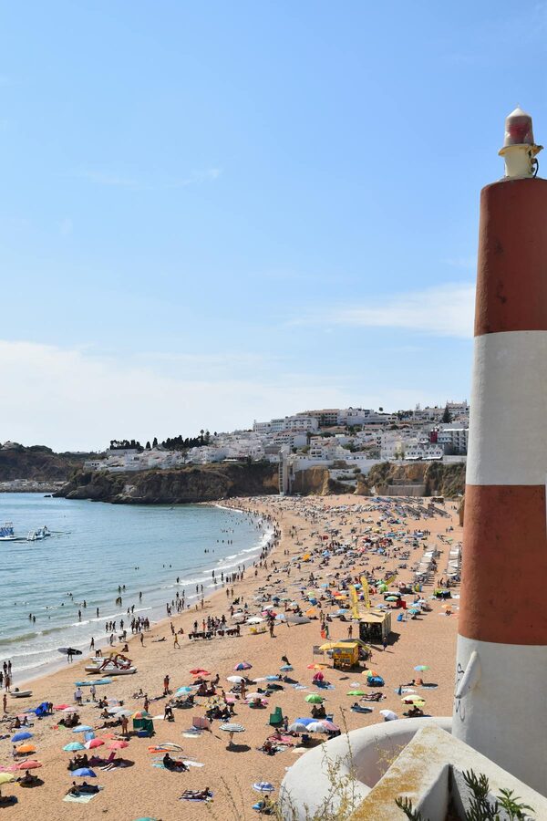 Colorful umbrellas and a lighthouse on Albufeira Beach on a bright summer day