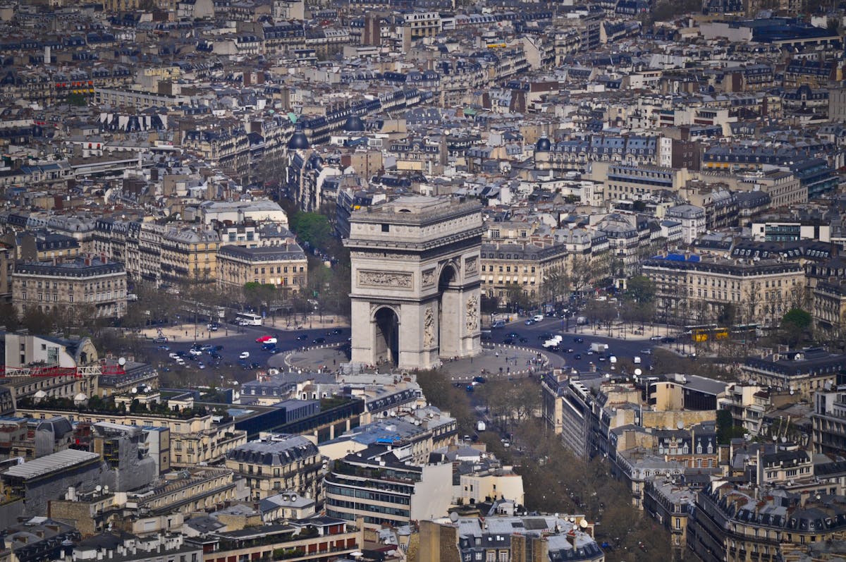 Aerial shot of the Arc de Triomphe surrounded by Parisian rooftops and radiating avenues