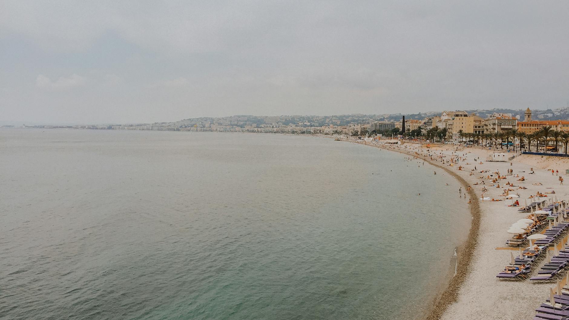 French Riviera turquoise waters lapping against a rocky shore with boats in the distance