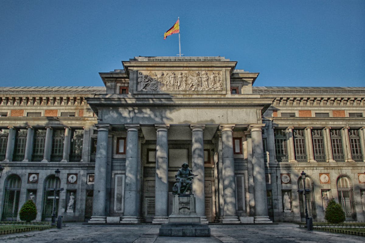 Exterior of the Prado Museum in Madrid with a clear blue sky and a statue in the foreground